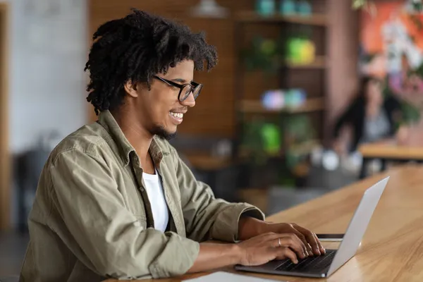 Jonge zwarte man typen op laptop tijdens het zitten aan tafel in Cafe — Stockfoto