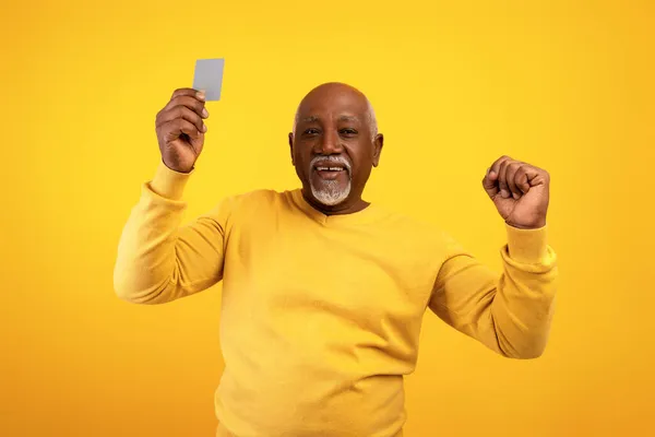 Літній афроамериканець показує кредитну картку і робить жест на помаранчевому фоні студії — стокове фото