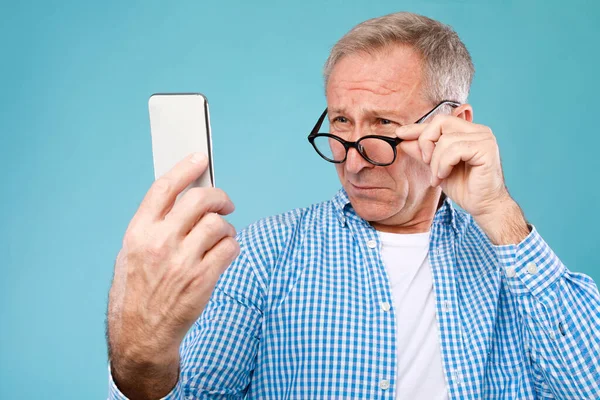 Ώριμος άνδρας που αλληθωρίζει χρησιμοποιώντας το κινητό τηλέφωνο, κοιτάζοντας την οθόνη — Φωτογραφία Αρχείου