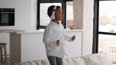 Childs Leisure 'da. Kablosuz kulaklıklı neşeli siyah çocuk kanepeye atlıyor.