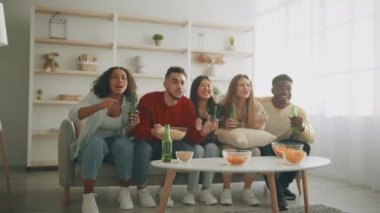 Bir grup genç çok ırklı arkadaş futbol taraftarı TV 'de bira ve aperatifle maç izliyor, golü kutluyor, zoom yapıyor