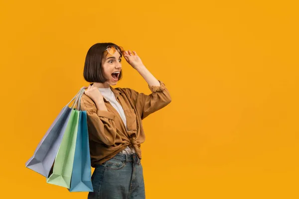 Sezónní prodejní koncept. Nadšení mladá žena drží světlé nákupní tašky a dívá se vzrušením na volné místo — Stock fotografie