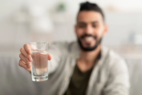 年轻的阿拉伯男子在家里镜头前拿着一杯清澈的水，有选择性地聚焦。健康概念 — 图库照片