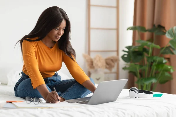 Mulher negra tomando notas sentado no laptop aprendizagem em casa — Fotografia de Stock