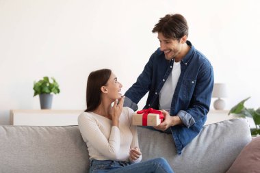 Neşeli bin yıllık Kafkas erkeği, sürpriz bir şekilde gülümseyen bir kadına oda içinde hediye veriyor.