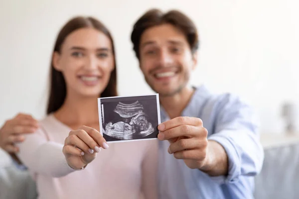 Sonriendo joven atractiva esposa europea y marido sostienen ultrasonido imagen escaneo bebé nonato en la habitación — Foto de Stock