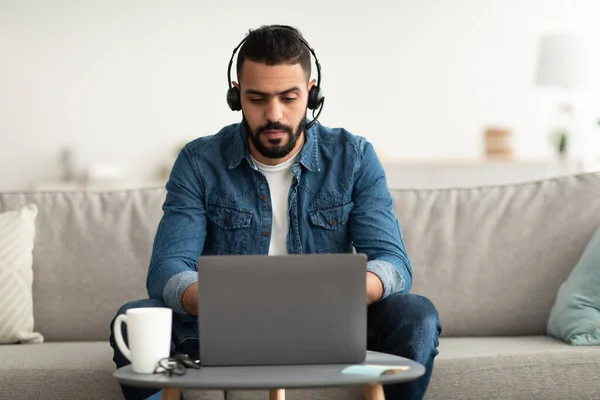 Arab w słuchawkach używając laptopa, pracując online, mając zdalną karierę, rozmawiając ze współpracownikami w sieci z domu — Zdjęcie stockowe