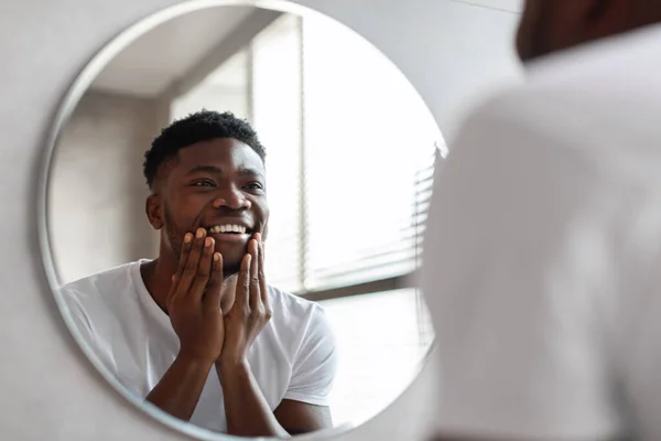 Feliz hombre afroamericano tocando la barbilla sin afeitar de pie en el baño — Foto de Stock