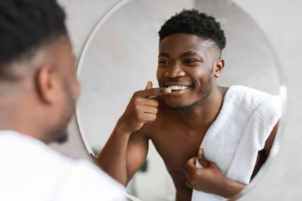 Negro hombre mirando su sonrisa en espejo en cuarto de baño — Foto de Stock