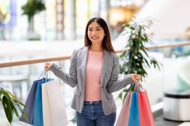 Güzel Asyalı bir kadının portresi. Elinde renkli hediye çantaları, alışveriş merkezinde alışveriş yapıyor.