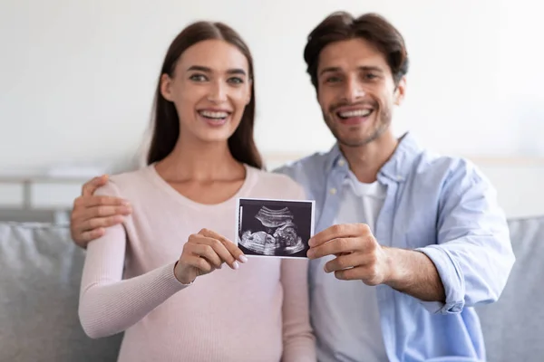 Feliz sorrindo milenar europeu homem e mulher segurando ultra-som foto do bebê na sala de estar — Fotografia de Stock