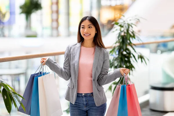 Porträtt av vacker ung asiatisk kvinna med färgglada presentpåsar i båda händerna, shopping i centrum — Stockfoto