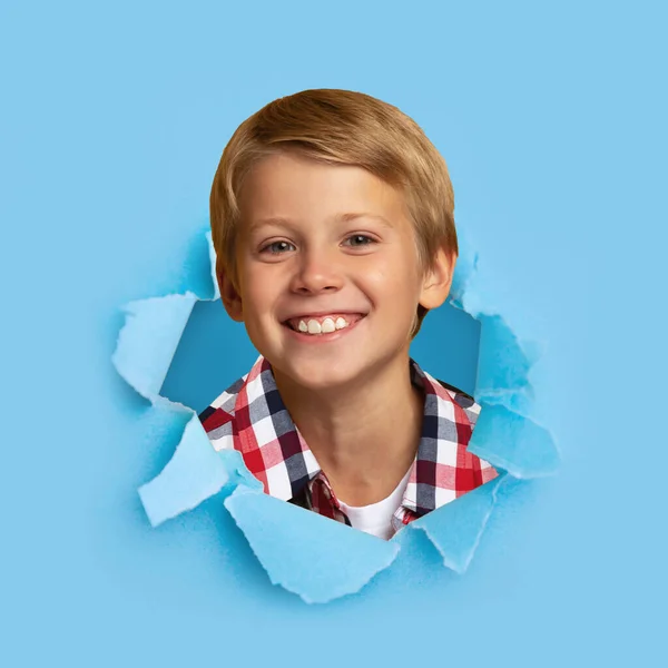Mosolygó európai jóképű szőke tini fiú tanuló néz át lyukon kék papíron, szabad hely, négyzet — Stock Fotó