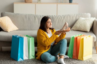 Uzaktan alışveriş konsepti. Yeni ayakkabısı olan heyecanlı Arap bayan, alışveriş torbalarının arasında oturuyor, alışverişlerden memnun.