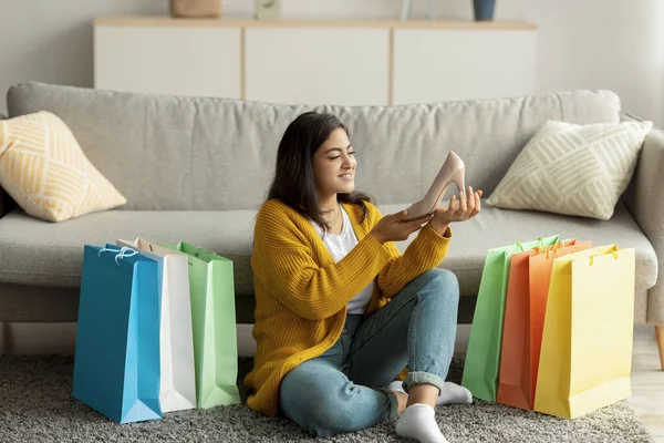Uzaktan alışveriş konsepti. Yeni ayakkabısı olan heyecanlı Arap bayan, alışveriş torbalarının arasında oturuyor, alışverişlerden memnun. — Stok fotoğraf