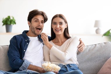 Gülümseyen neşeli, mutlu, genç Avrupalı çift patlamış mısır yiyor ve komik film izliyor.