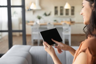 Boş siyah ekranlı tablet kullanan genç bayan, evden internet üzerinden çalışıyor veya çalışıyor, uygulama ya da web sitesi için modelleme yapıyor