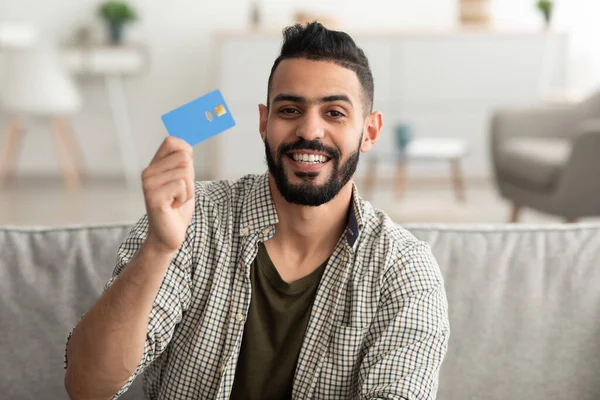 Portrét pozitivního mladého Araba ukazujícího kreditní kartu, nakupování z domova — Stock fotografie