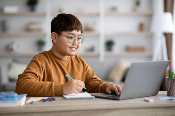 Inteligentny azjatycki chłopiec siedzi przed laptopem, odrabiając lekcje — Zdjęcie stockowe