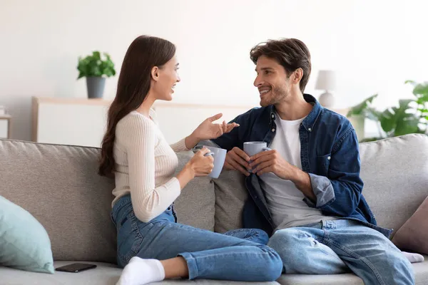 새 천 년을 맞이하는 남성 과 여성은 소파에 앉아 뜨거운 음료를 마시고 거실에서 대화를 나누며 — 스톡 사진