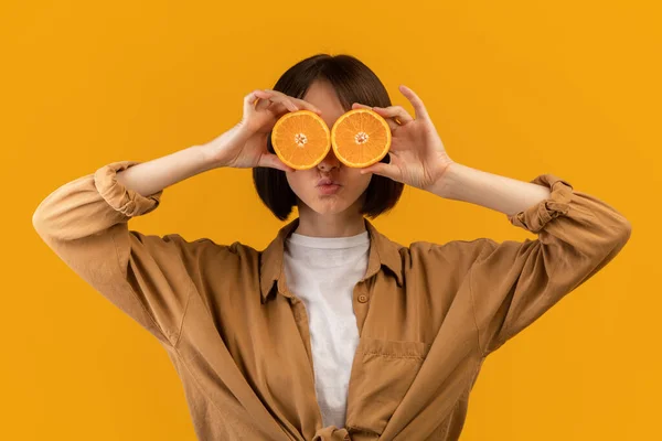 Παιχνιδιάρα καυκάσια κυρία καλύπτει το μάτι της με πορτοκαλί ημίχρονα, ποζάροντας σε κίτρινο φόντο στούντιο — Φωτογραφία Αρχείου