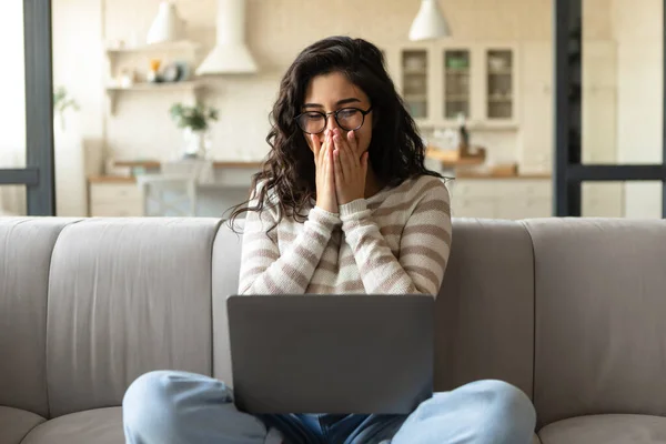 Giovane donna caucasica guardando lo schermo del computer portatile, ridendo, coprendo la bocca, guardando film divertenti sul pc a casa — Foto Stock