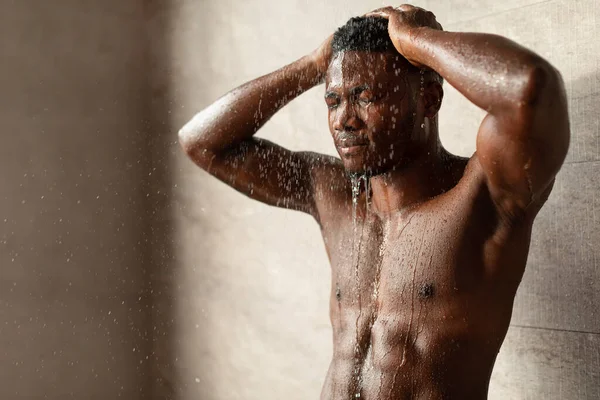 Negro hombre con ojos cerrado tomando ducha lavando cabeza interior — Foto de Stock