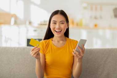 Siber alışveriş, mevsimsel satış konsepti. Cep telefonu ve kredi kartıyla online mağazadan mal alan aşırı neşeli Asyalı kadın.
