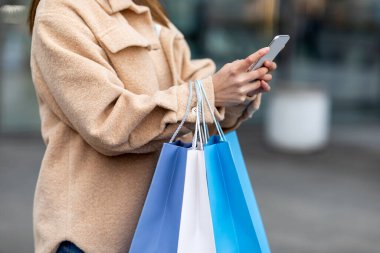 İnternetten soğuk mevsim alışverişi yapan tanınmayan Asyalı kadın, açık havada cep telefonu kullanıyor.