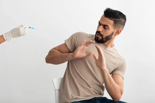 Sin vacunación. Asustado hombre árabe gesto parada al médico que ofrece jeringa con vacuna covid, negándose a ser vacunado —  Fotos de Stock