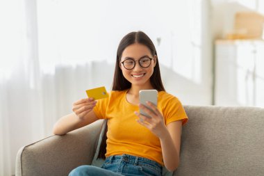 İnternetten alışveriş, uzaktan bankacılık konsepti. Gözlüklü mutlu Asyalı bayan internetten satın alıyor.