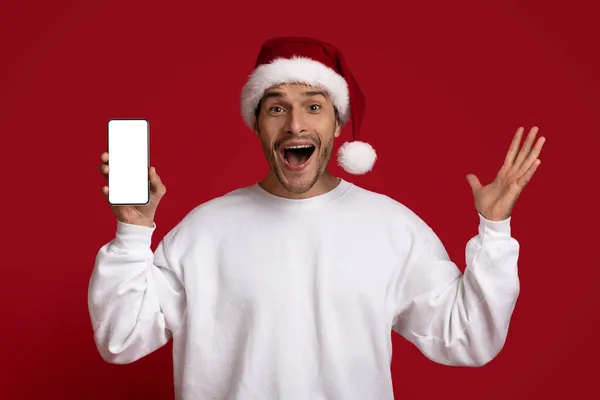 令人惊奇的报价。《圣诞老人帽》里兴奋的家伙拿着装有空白屏幕的智能手机 — 图库照片
