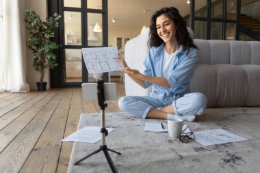 Akıllı telefon webcam 'inde doküman gösteren güzel genç bir kadın, evde online iş toplantısına katılıyor.