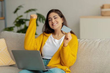 Kredi kartı ve dizüstü bilgisayarı olan neşeli genç Arap bayan çevrimiçi piyangoda kazanıyor, evden büyük bir satış yapıyor.