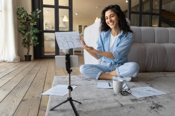 Akıllı telefon webcam 'inde doküman gösteren güzel genç bir kadın, evde online iş toplantısına katılıyor.