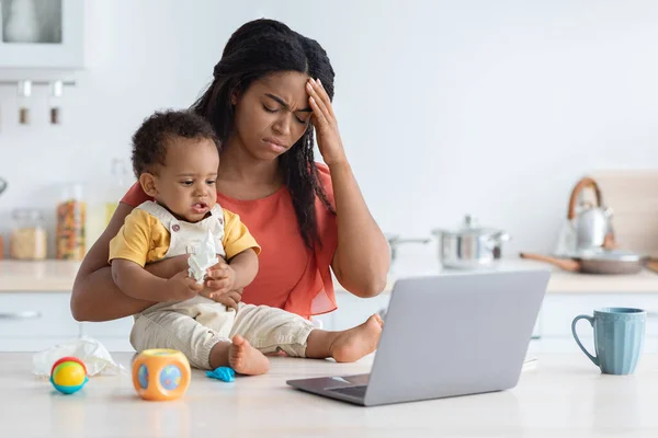 Материнский стресс. Молодая чернокожая мать страдает головной болью, сидя со своим младенцем — стоковое фото