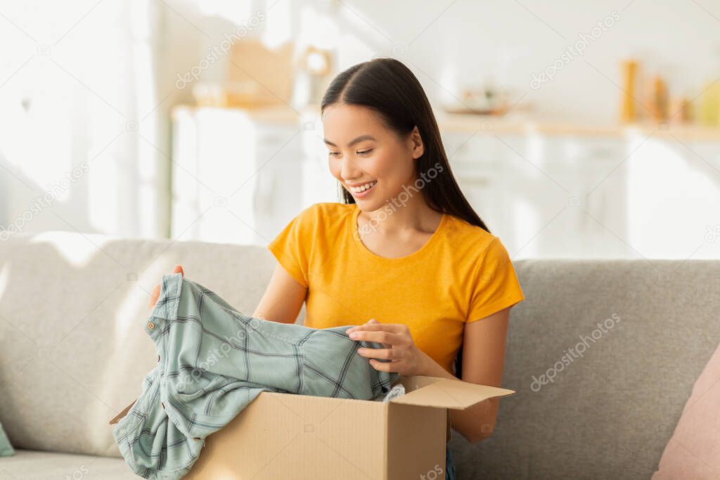 Delivery concept. Satisfied female buyer opening and unboxing parcel cardboard box, sitting on sofa in living room