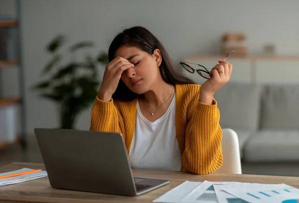Mulher árabe exausta que sofre de dor de cabeça, usando laptop e trabalhando em casa, removendo óculos e esfregando os olhos — Fotografia de Stock