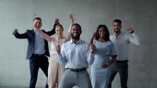 Éxito empresarial. Grupo de colegas multiétnicos saltando sobre la pared gris, disfrutando de un trato exitoso, bailando a cámara — Vídeos de Stock