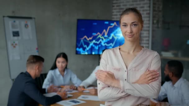 Självsäker medelålders kvinna manager ler mot kameran, poserar på moderna kontor, kollegor möte på bakgrunden — Stockvideo