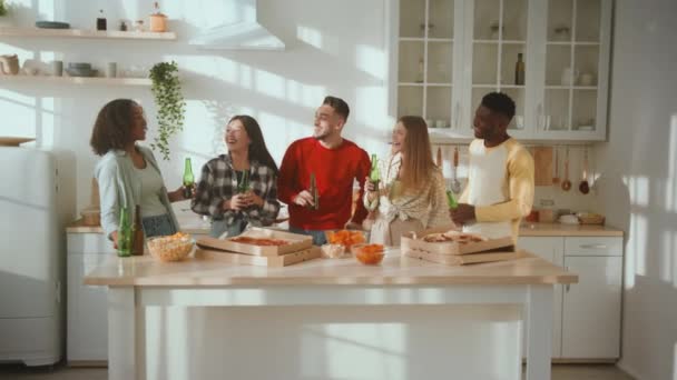 Feliz festa da casa. Grupo de jovens amigos diversos comemorando os fins de semana juntos, batendo com garrafas de cerveja na cozinha — Vídeo de Stock