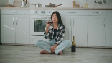 Stres ve zararlı alışkanlıklar. Depresyonda olan Asyalı bir kadın mutfakta tek başına oturmuş kırmızı şarap içiyor.