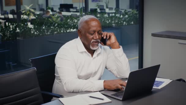 Black Mature Businessman Berbicara di Cellphone Dan menggunakan Laptop Computer In Office — Stok Video