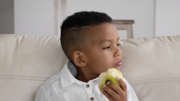 Закрыть портрет маленького черного мальчика, поедающего зеленое яблоко дома — стоковое видео
