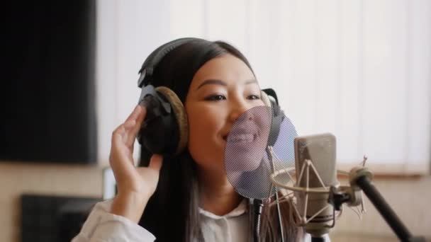 Asijské ženské hudebnice nosící sluchátka zpívající píseň na mikrofon v hudebním studiu — Stock video