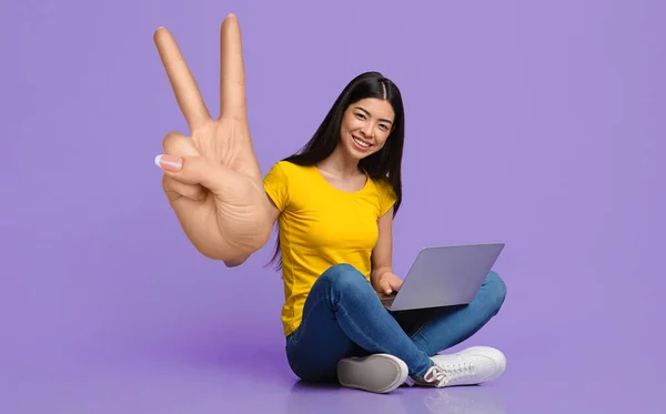Trabajo remoto o educación. Sonriente joven asiática sentada con portátil, mostrando gran paz o gesto de victoria — Foto de Stock
