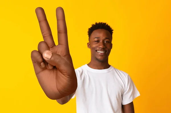 Genç Afrikalı Amerikalı adam kameraya gülümsüyor ve turuncu arka planda büyük bir barış ya da zafer hareketi gösteriyor. — Stok fotoğraf
