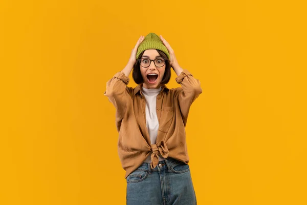 Geschokte vrouw tilt handen omhoog en raakt hoofd over gele studio achtergrond, emotionele dame uiten verbazing — Stockfoto