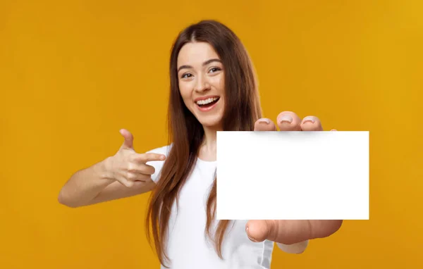 Vrolijke jongedame wijzend naar leeg visitekaartje, glimlachend naar camera op oranje studio achtergrond, mockup — Stockfoto