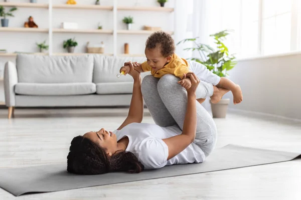 Sport tevékenységek a babával. Fekete anya gyakorlása a csecsemő fiú otthon — Stock Fotó